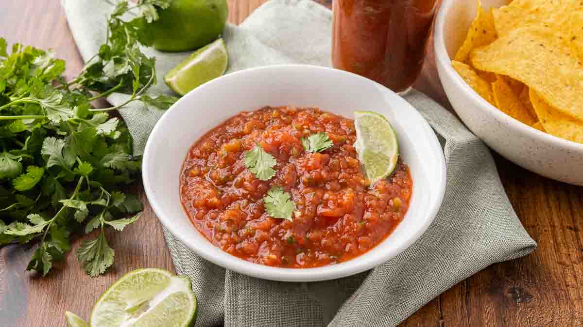 A white bowl full of fermented salsa garnished with cilantro and a wedge of lime.