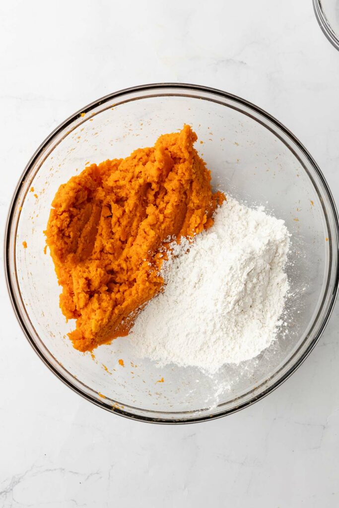 A glass bowl with mashed sweet potato, salt and flour.