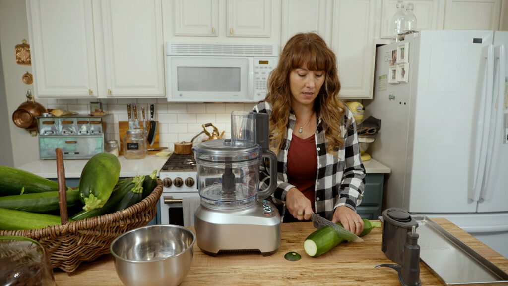 A woman chopping a zucchini on a cutting board.