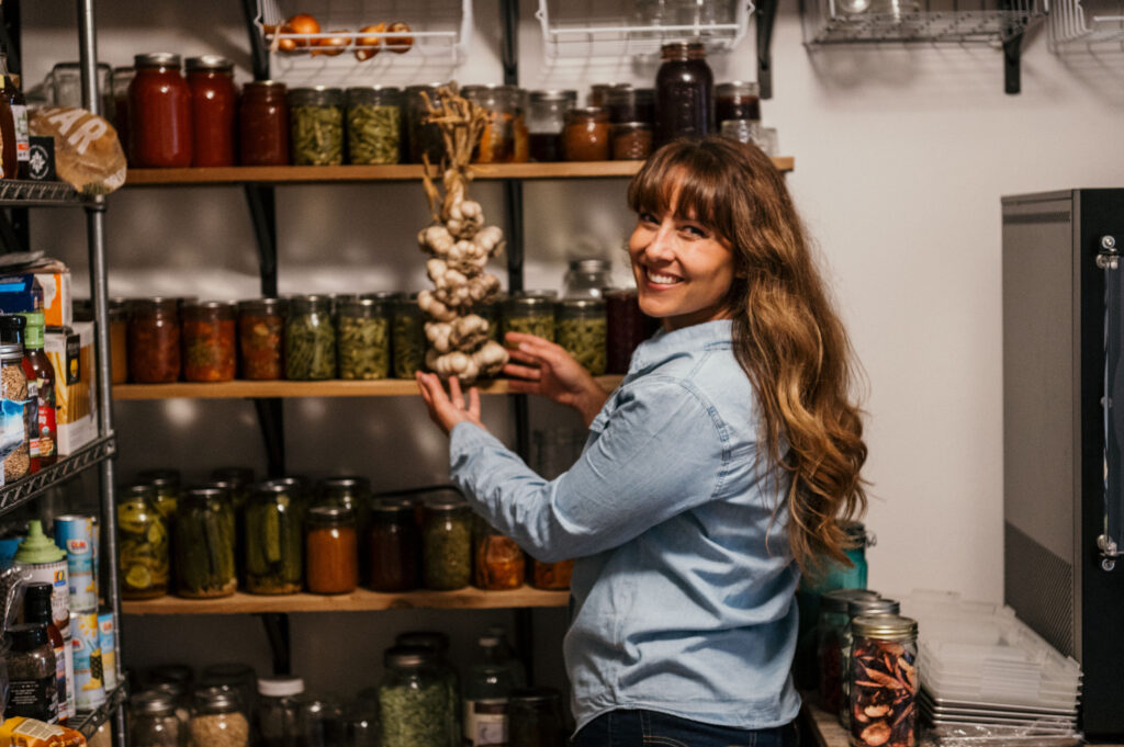 A woman in her pantry with shelves of preserved food.