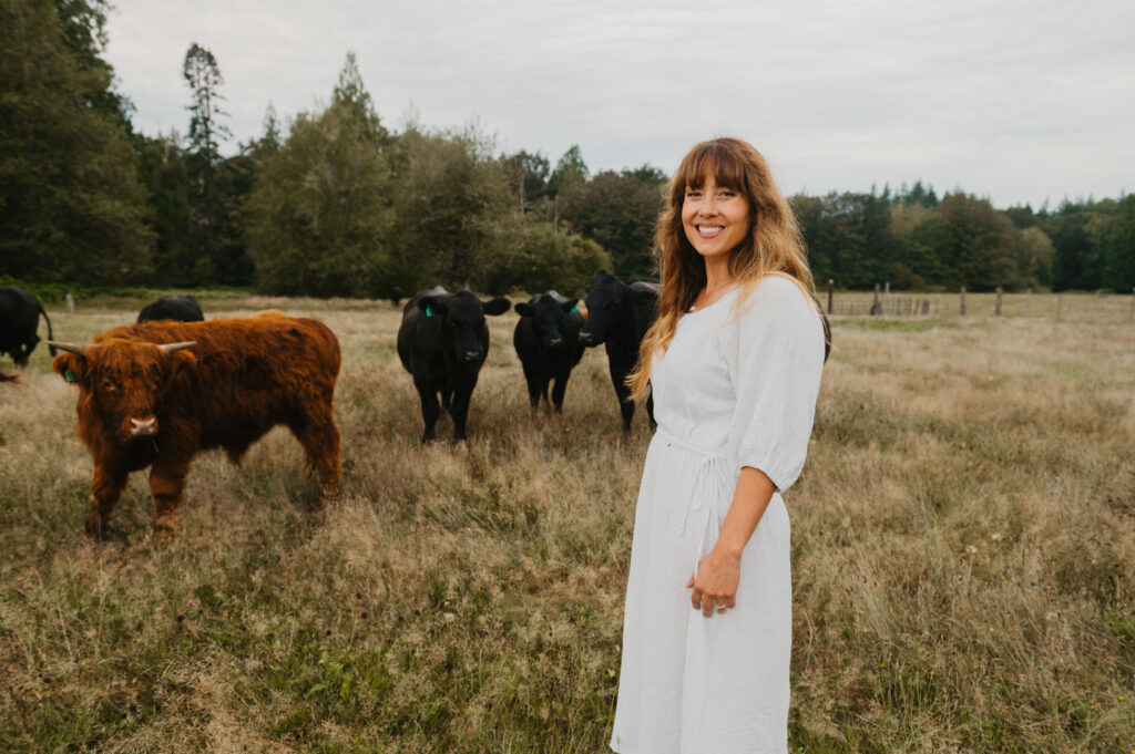 A woman in a white dress with cows in a field in the background.