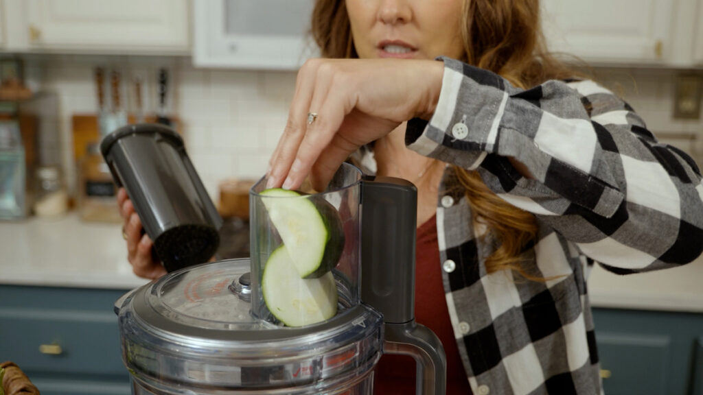 Zucchini going into a food processor to get shredded.