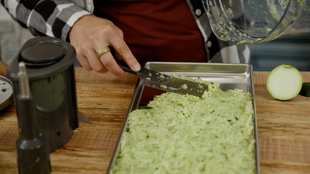 A woman spreading shredded zucchini onto a freeze dryer tray.