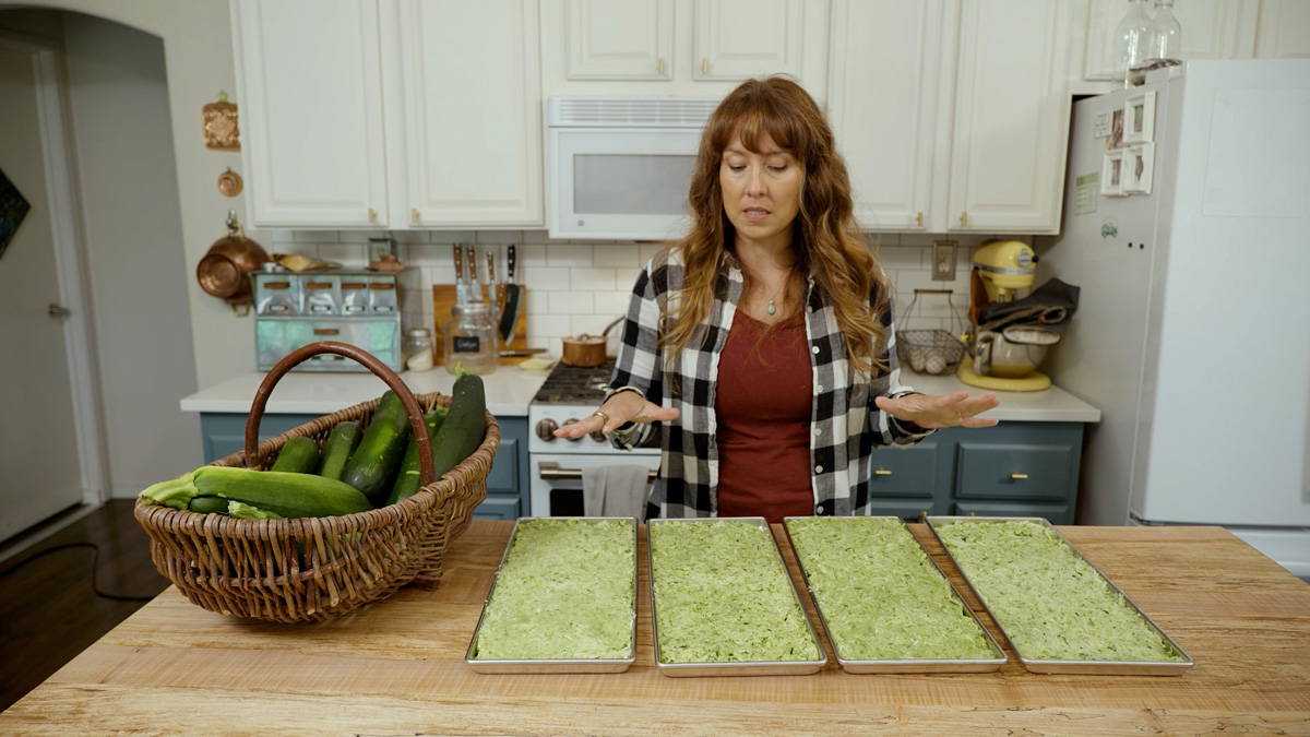 A woman in the kitchen with four trays of freeze dried zucchini.