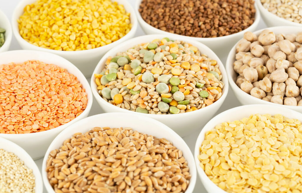 White bowls filled with various beans, lentils and grains.