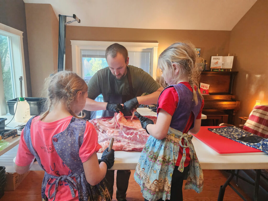 A man and his two daughters butchering a cow in their living room.