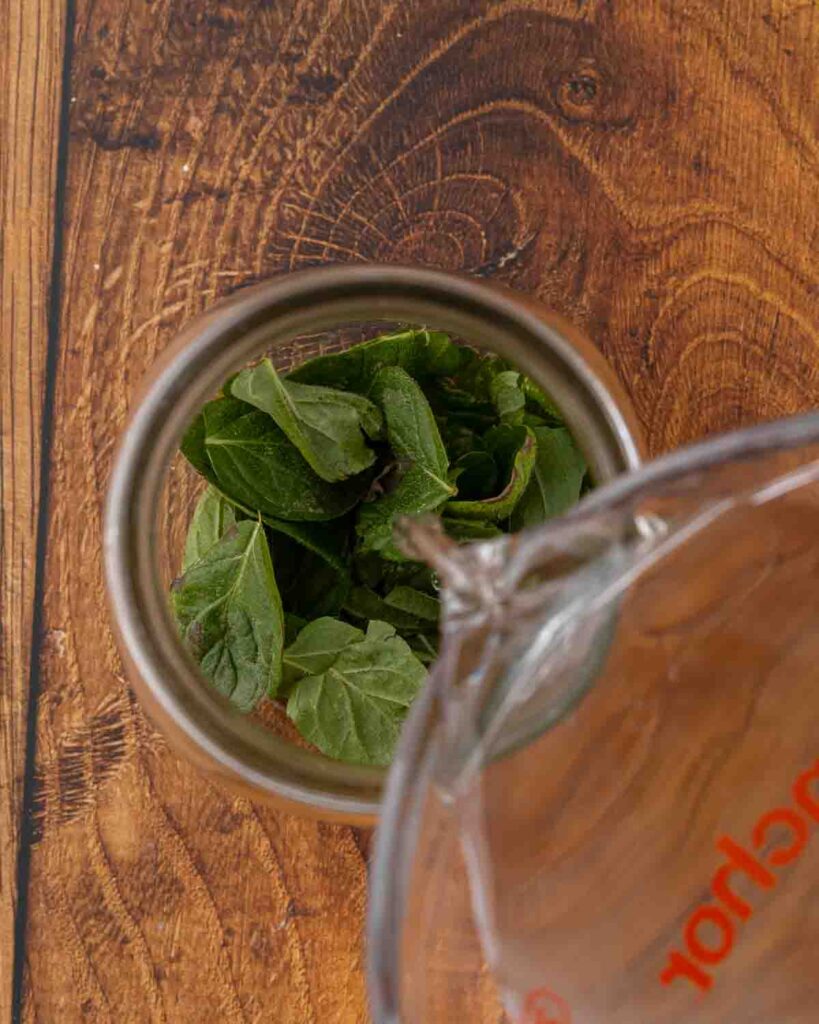 Pouring vodka into a jar filled with mint.