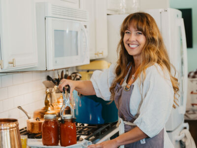 Woman standing at stove putting jars of home canned tomato sauce into pressure canner