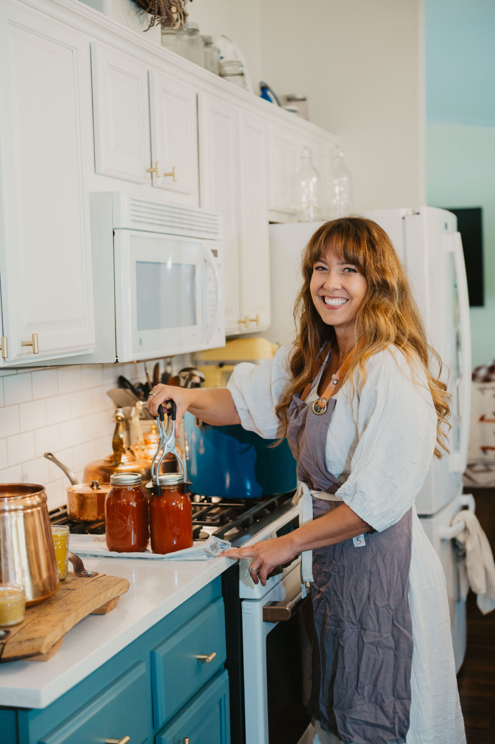 Woman standing at stove putting jars of home canned tomato sauce into pressure canner