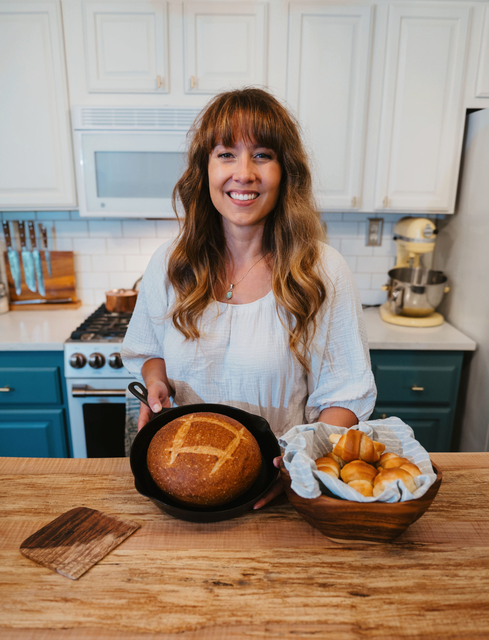 Woman holding a fresh artisan loaf and homemade crescent rolls in a basket in the kitchen