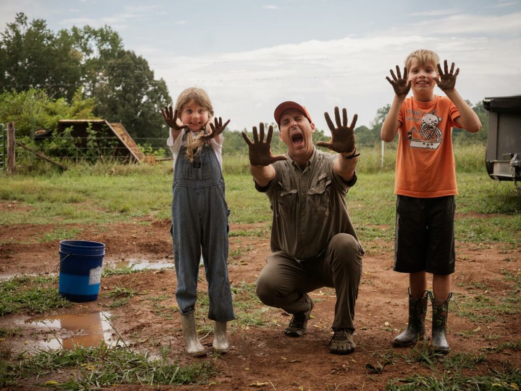 A father and two kids with muddy hands.