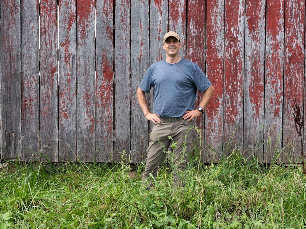 A man in a hat standing in front of a barn.