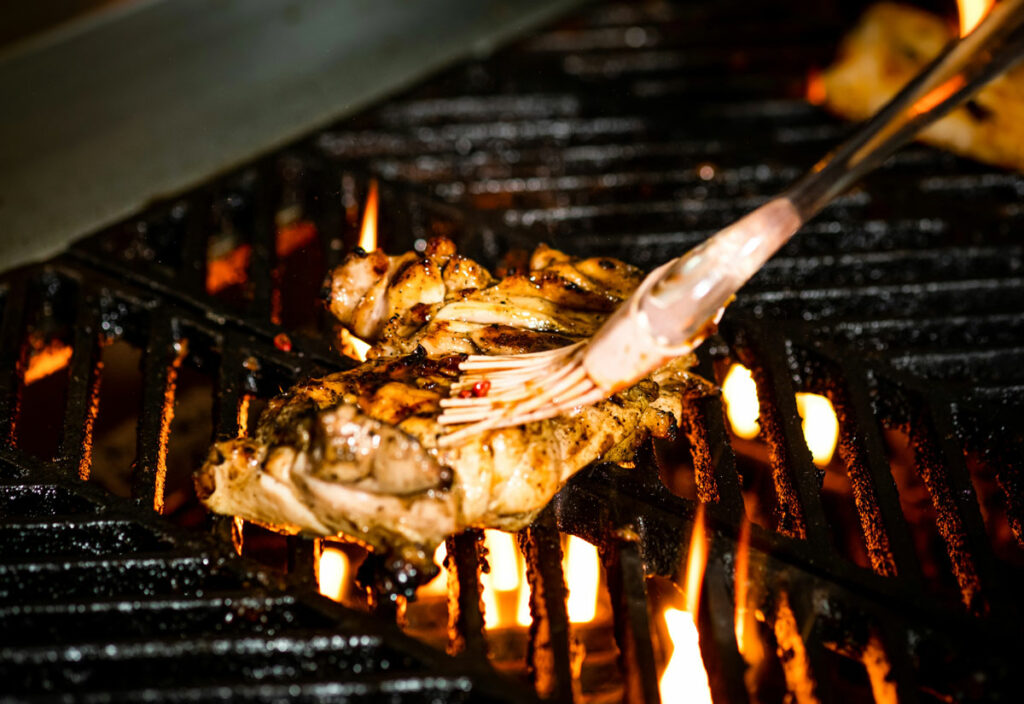 Chicken being grilled on an open flame and brushed with herb oil.