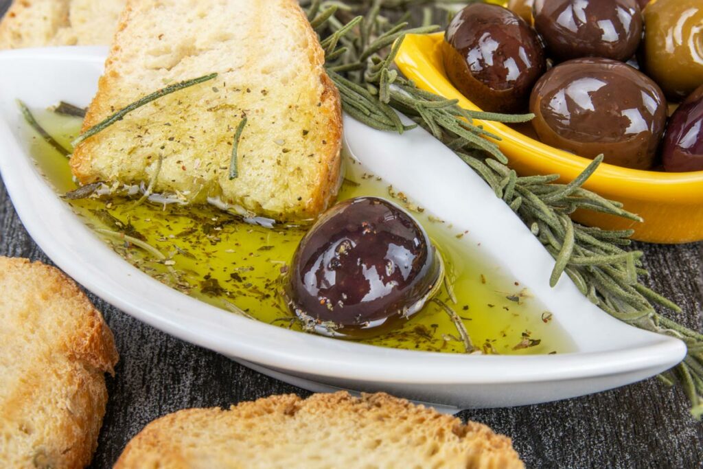 Herb infused olive oil in a shallow plate with bread being dipped.