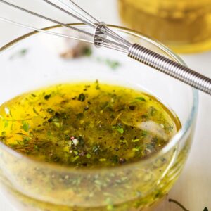 Herb oil in a glass bowl with whisk.