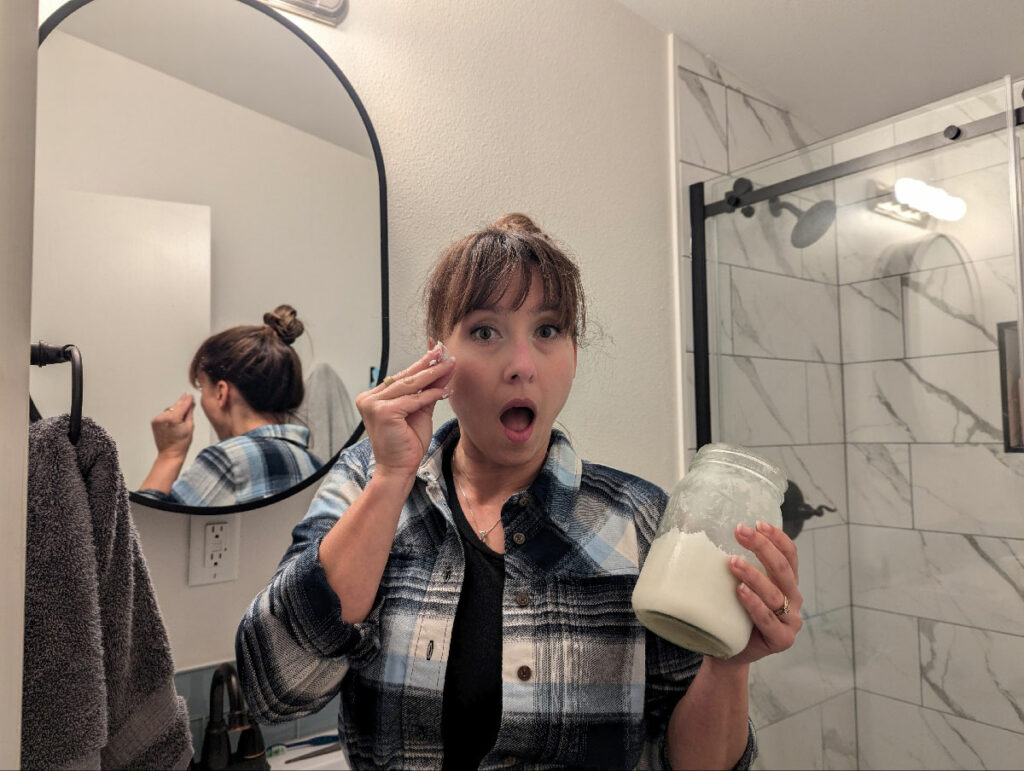 A woman in the bathroom putting lard on her face.