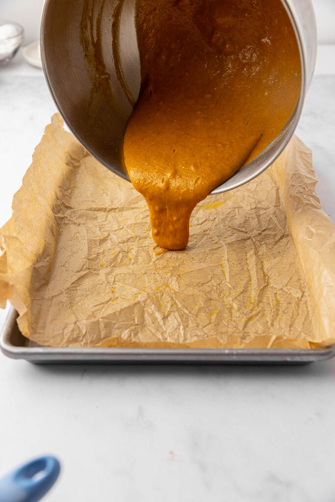 The batter for a pumpkin roll cake being poured into a 9x13 sheet pan.