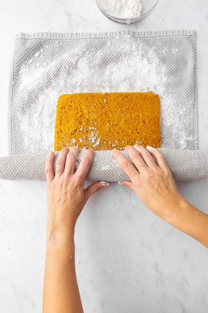 A pumpkin roll cake being rolled in a tea towel.