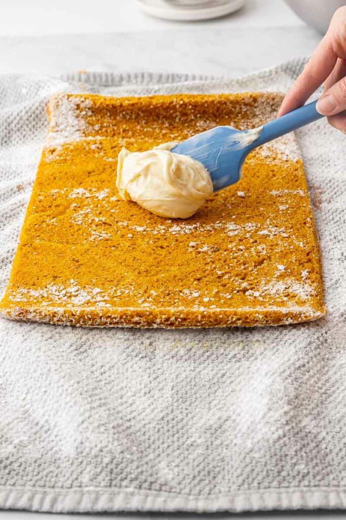 Frosting being spread on a pumpkin roll cake.