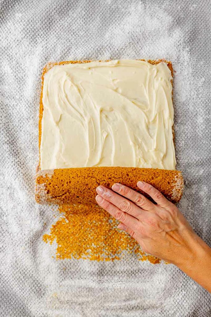 Pumpkin roll being rolled up with frosting in the center.