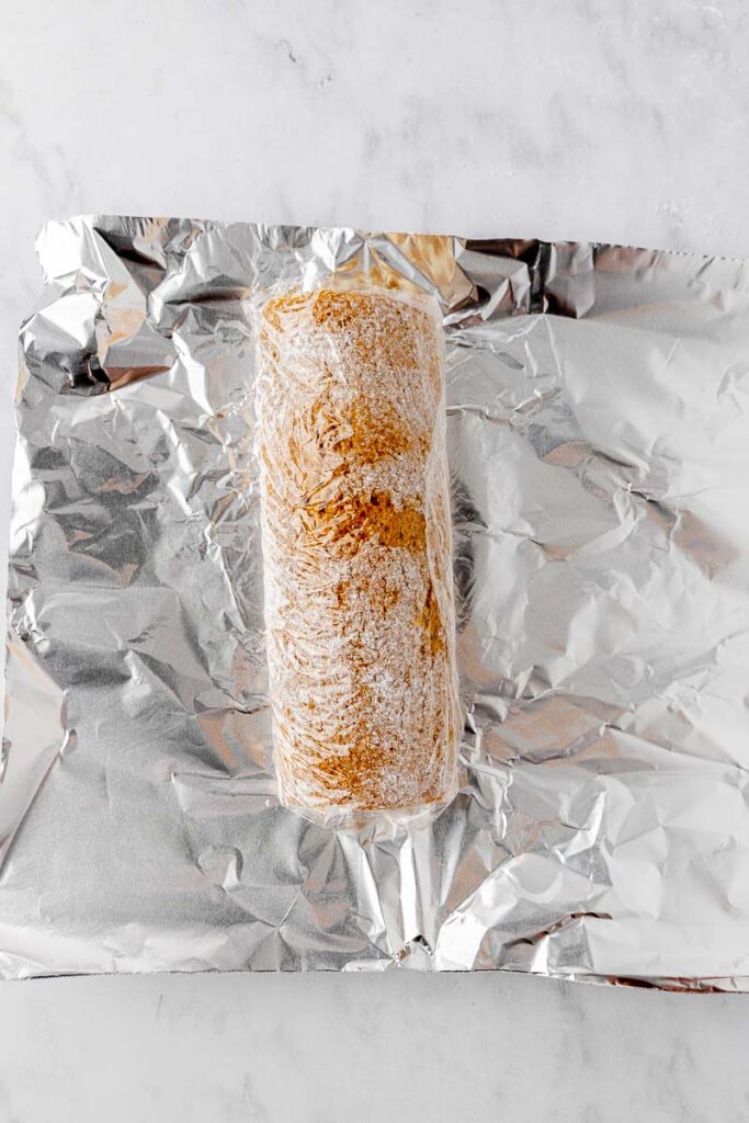 A pumpkin roll wrapped in plastic wrap on top of tinfoil.