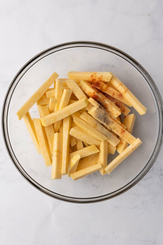 Sliced rutabaga in a glass bowl with seasonings and oil.