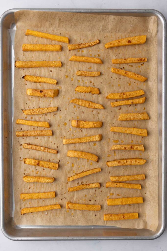 Baked sliced rutabaga fries on a parchment lined baking sheet.