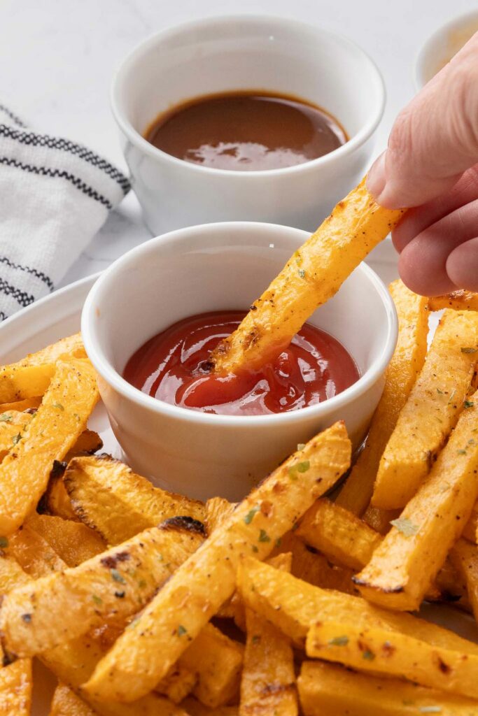 A rutabaga fry being dipped into ketchup.