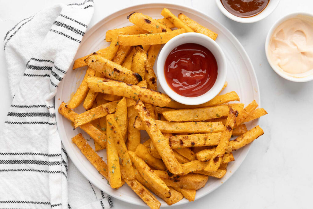 Rutabaga fries on a white plate with dipping sauces.