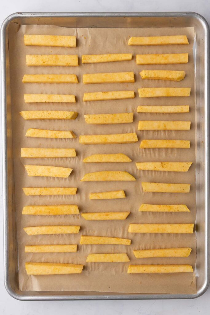 Seasoned and sliced rutabaga on a parchment lined baking sheet.