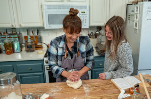 Mom showing a daughter how to knead dough in the kitchen