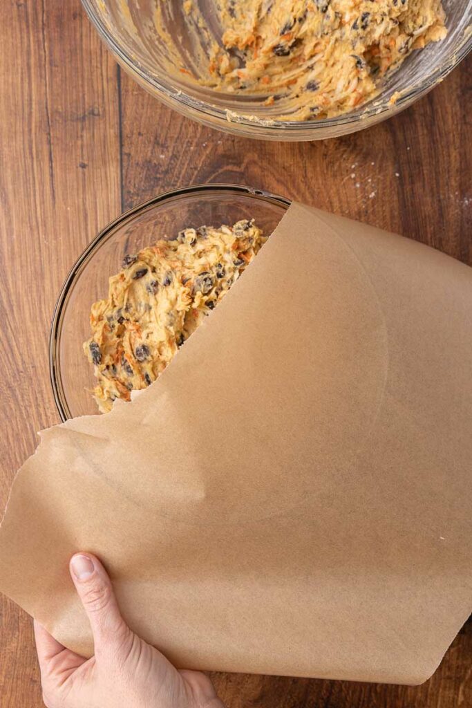 Christmas pudding batter being covered with parchment paper.