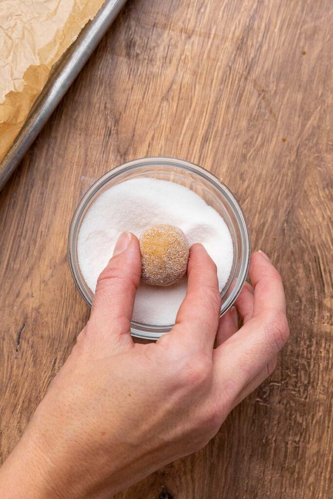 A ball of molasses cookie dough being rolled in sugar.