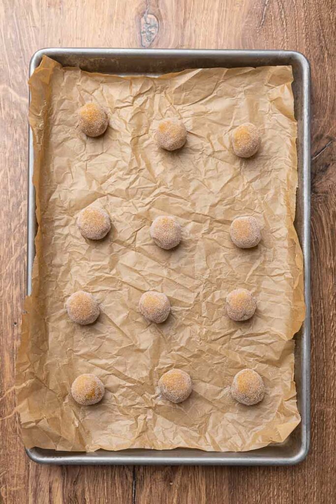 Molasses cookie dough in balls on a parchment paper lined baking sheet.