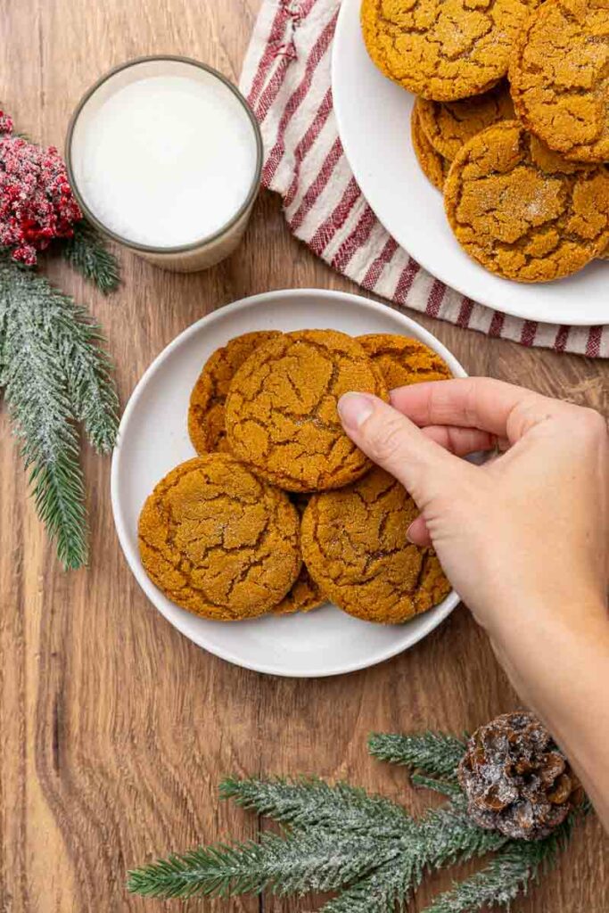 A hand reaching for a molasses cookie from a plate full.