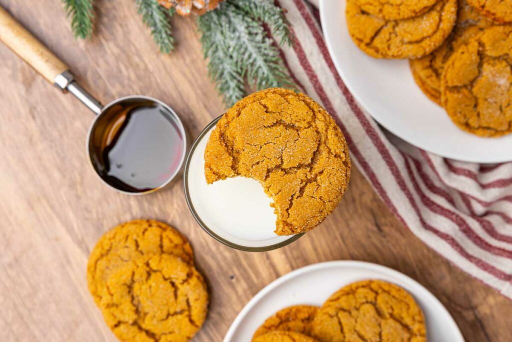 Molasses cookies with one taken a bite out on top of a glass of milk.