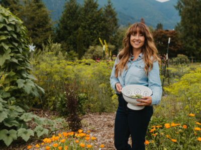 A woman in the garden with a colander, harvesting vegetables.