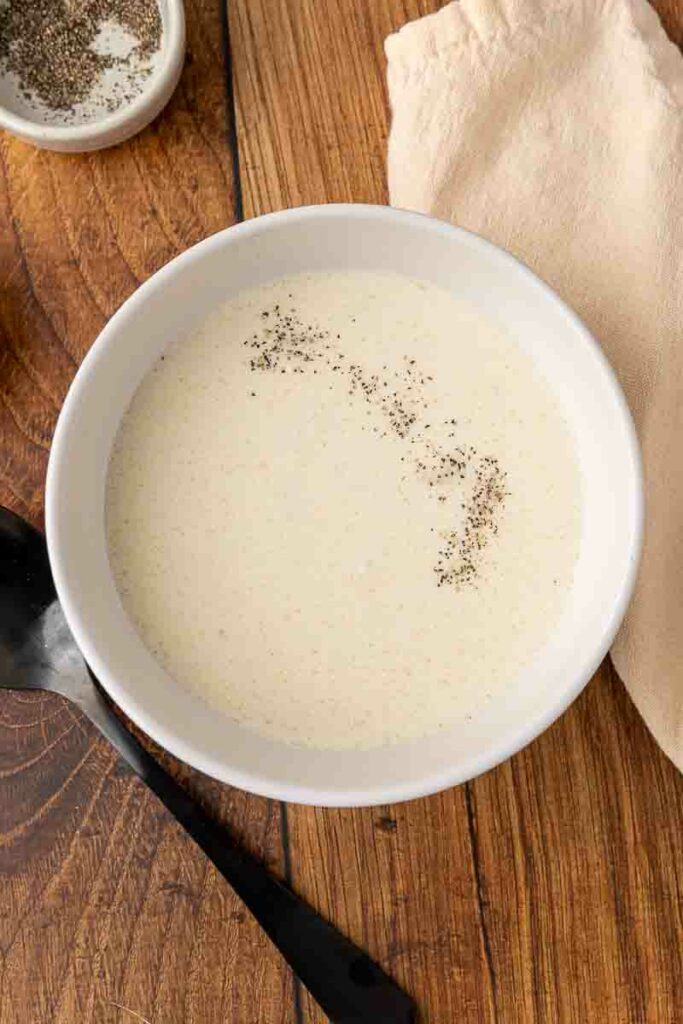 A bowl of cream of chicken soup on a wooden counter.