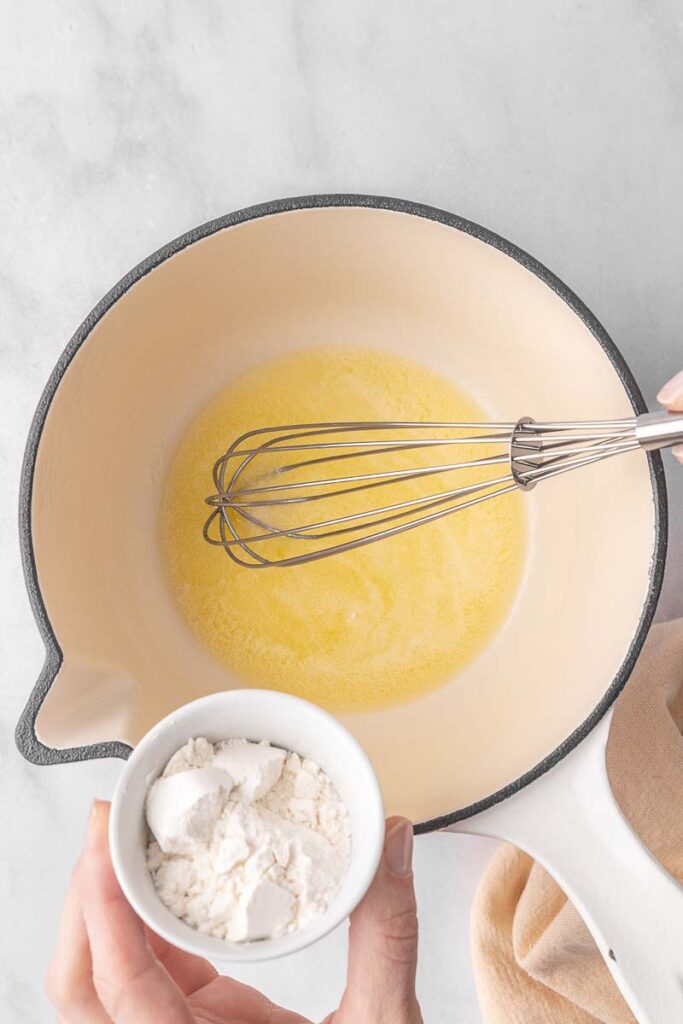 Flour being poured into a pot with melted butter to create a roux.