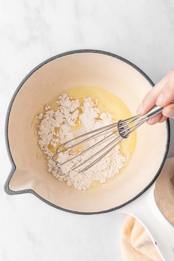 Flour being whisked into melted butter in a large pot.