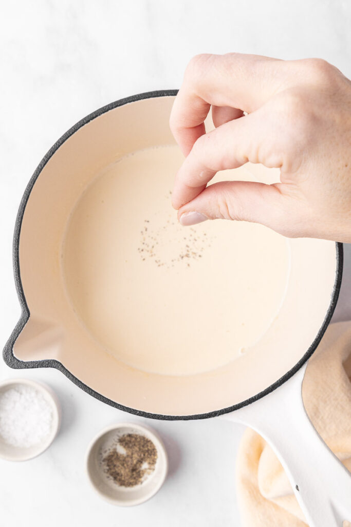 A pinch of black pepper being added to cream of chicken soup.