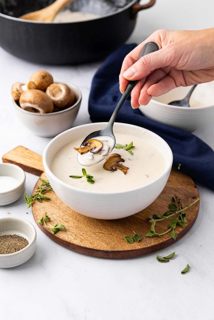 A bowl of cream of mushroom soup with someone taking a spoonful.