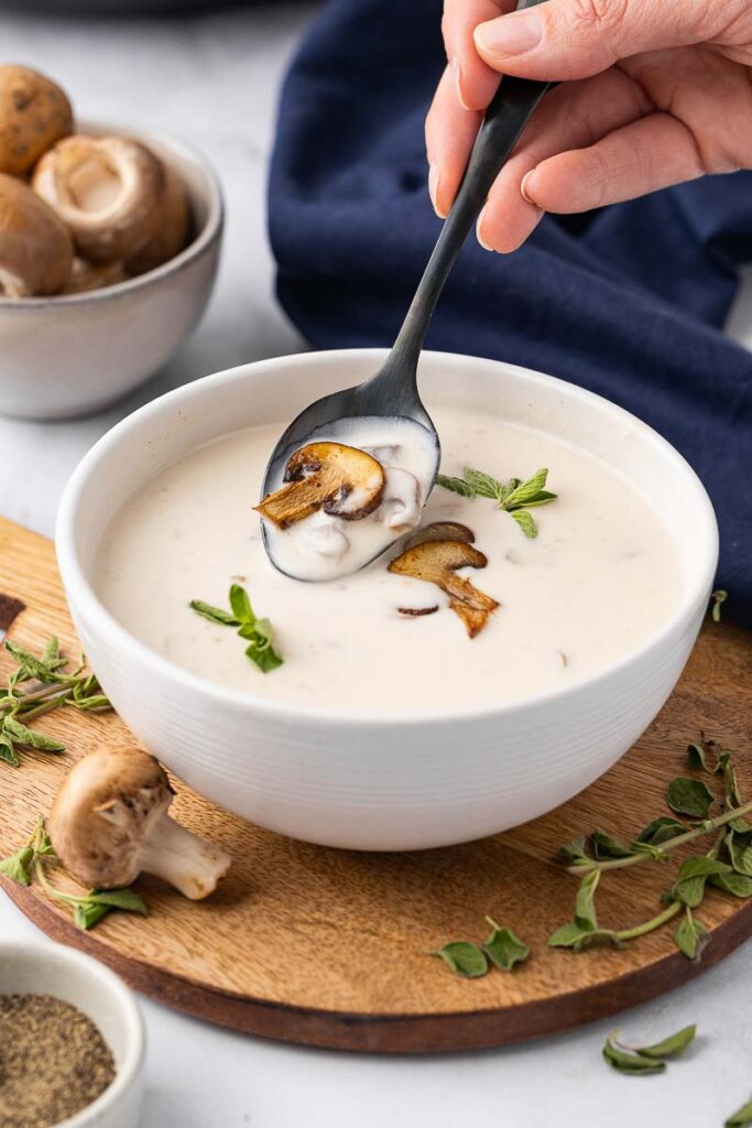 A bowl of cream of mushroom soup with someone taking a spoonful.