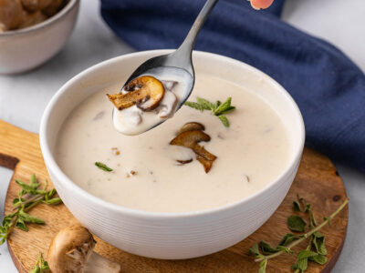 A bowl of cream of mushroom soup with someone taking a spoonful.