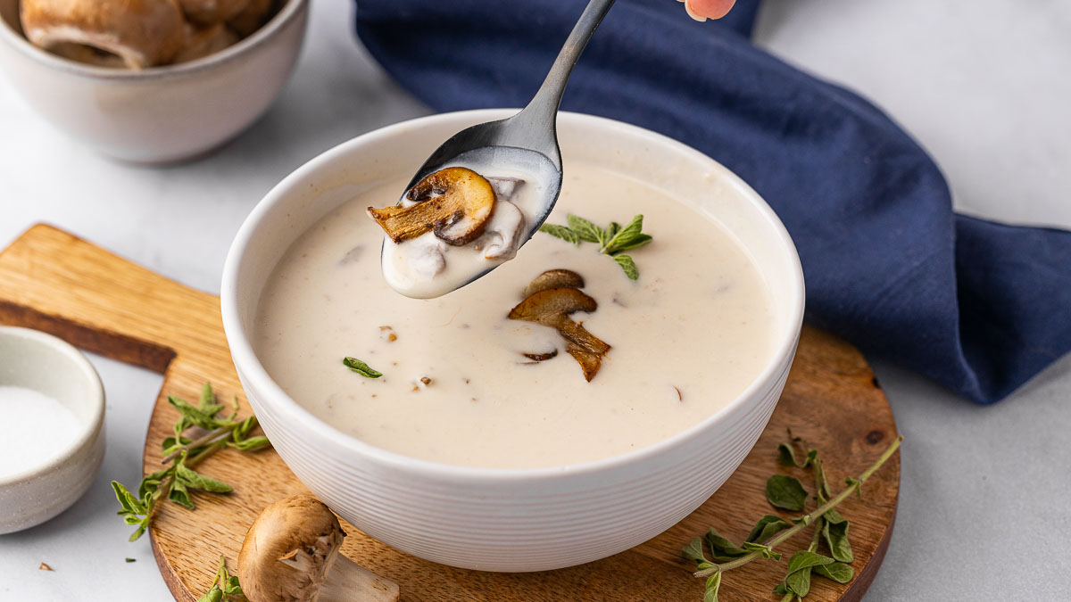 A bowl of cream of mushroom soup with someone taking a spoonful.