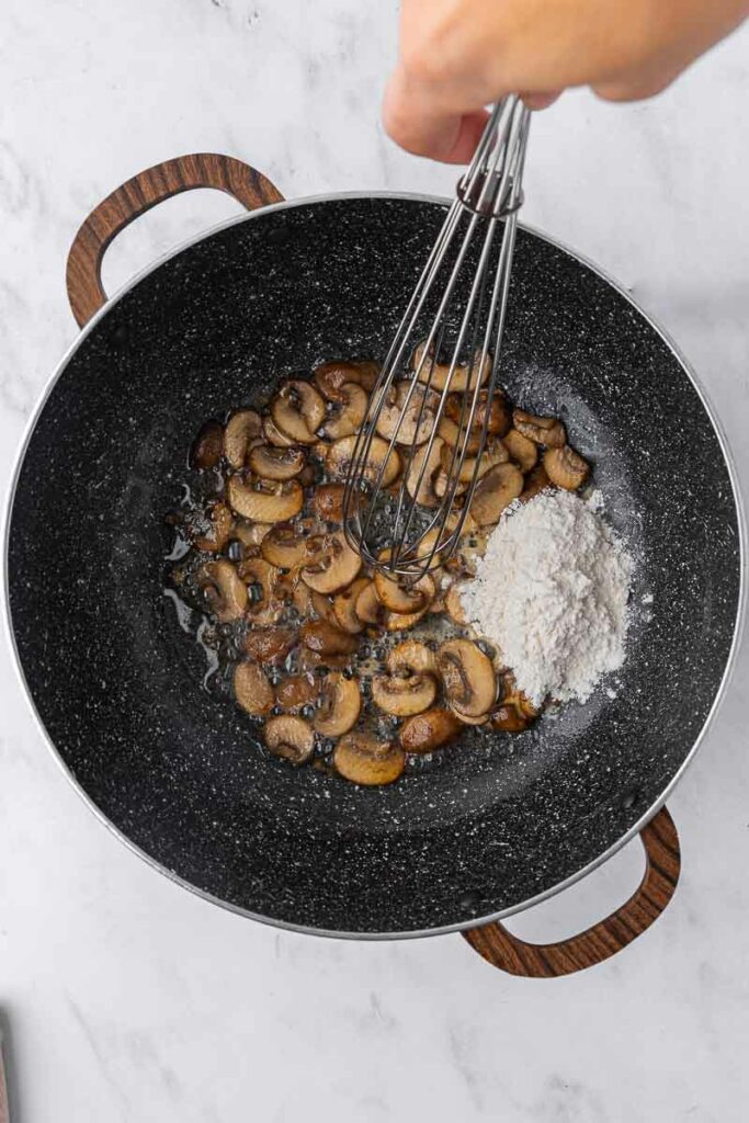 Flour being added to sauteed mushrooms.