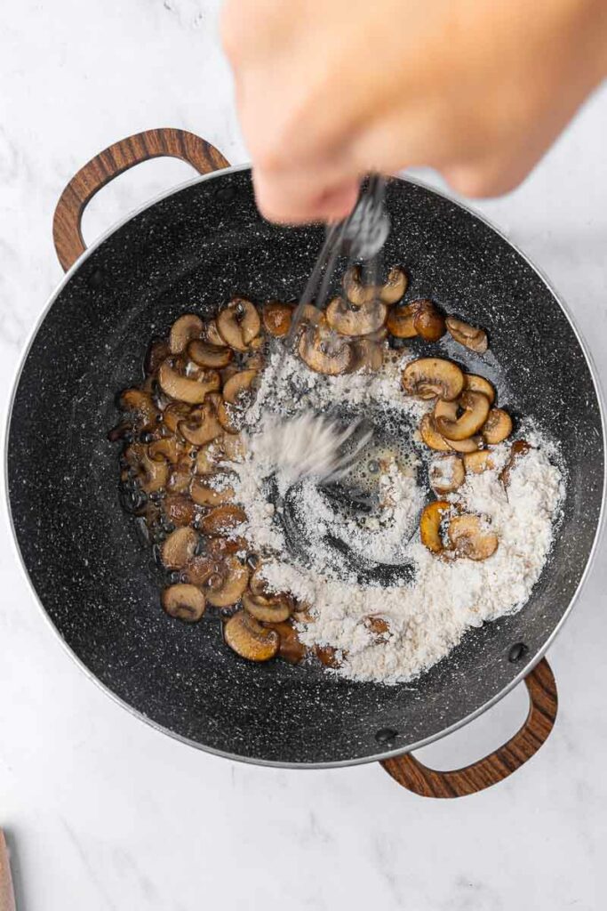 Flour being added and stirred in with sauteed mushrooms.