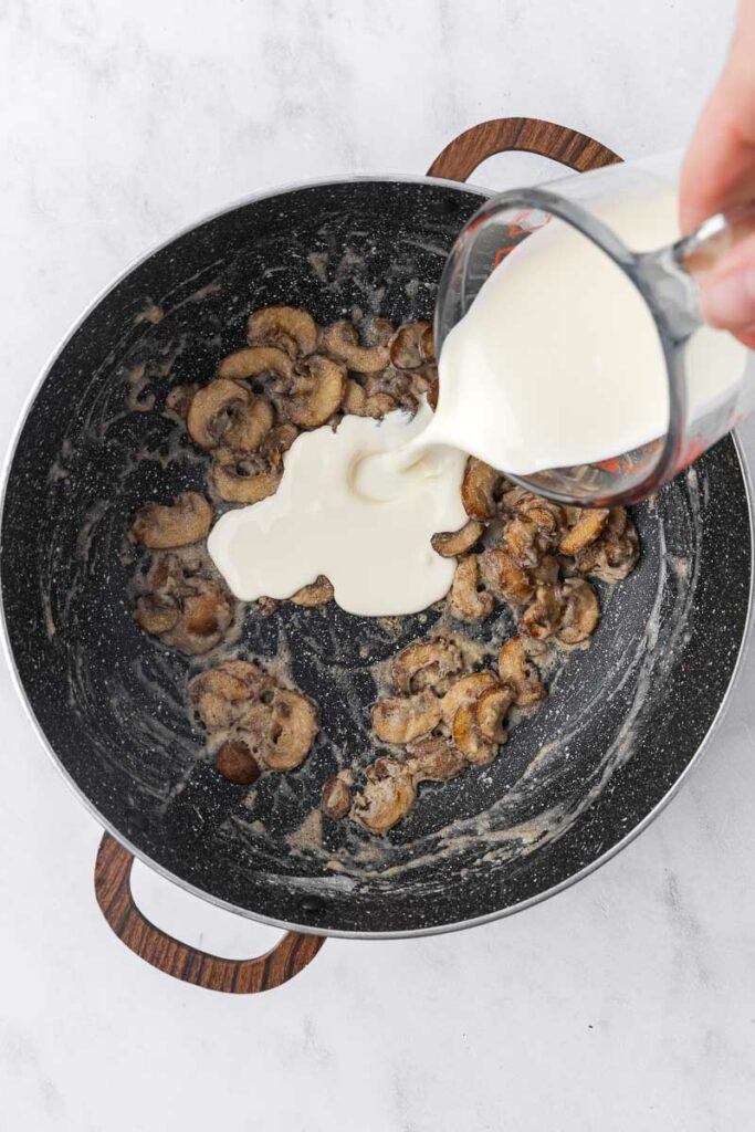 Cream being added to sauteed mushrooms with flour.