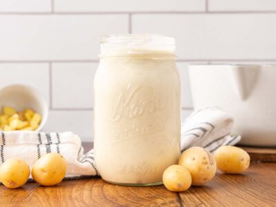 A jar of homemade cream of potato soup with potatoes on the counter.