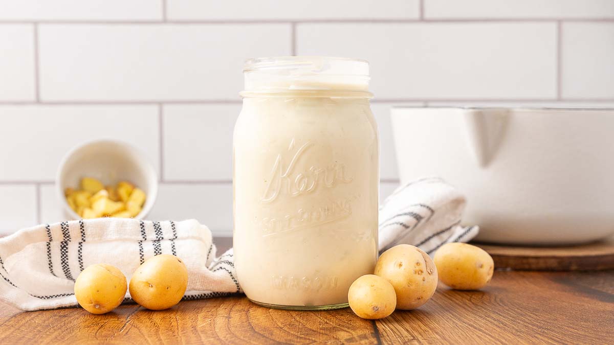 A jar of homemade cream of potato soup with potatoes on the counter.